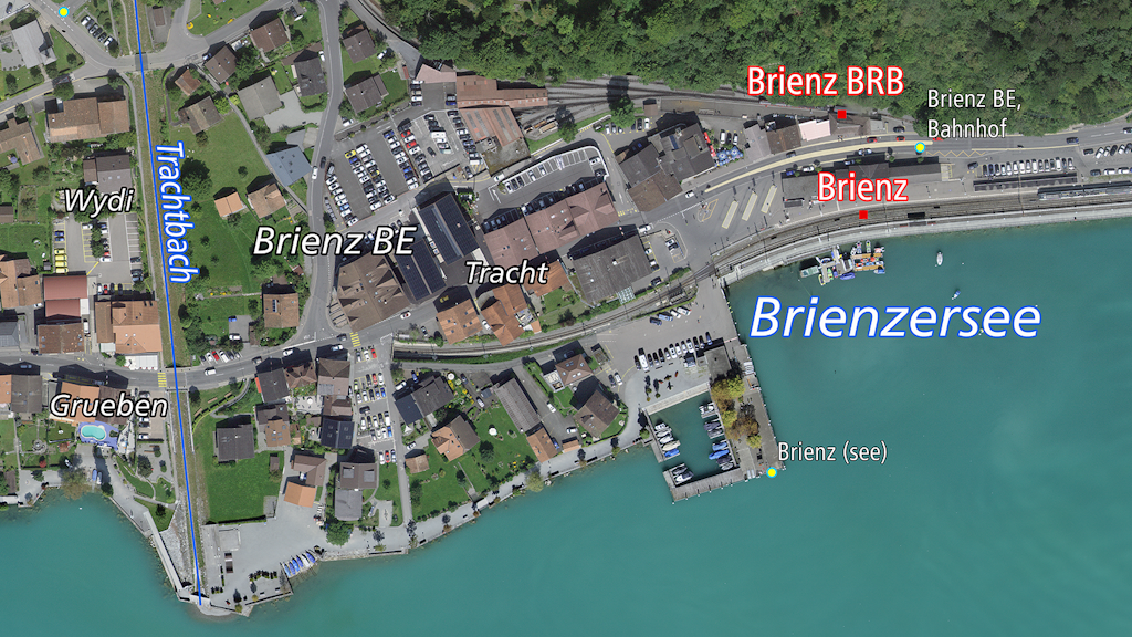 L'immagine mostra una veduta aerea di Brienz BE con il paese, la stazione ferroviaria e il lago di Brienz. 