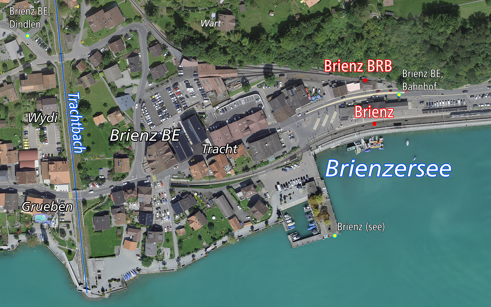 Das Bild zeigt eine Luftaufnahme von Brienz BE mit dem Dorf, dem Bahnhof und dem Brienzersee. 