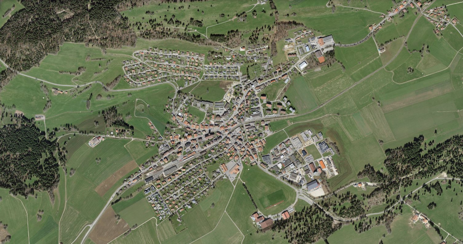 L'image montre une vue aérienne de Saignelégier (JU) avec un environnement généreux.