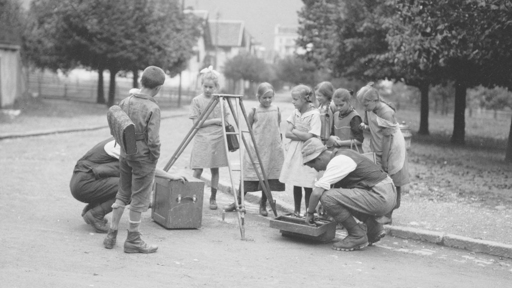 Children on their way to school take an interest in the work of surveyors setting up their theodolites. 
