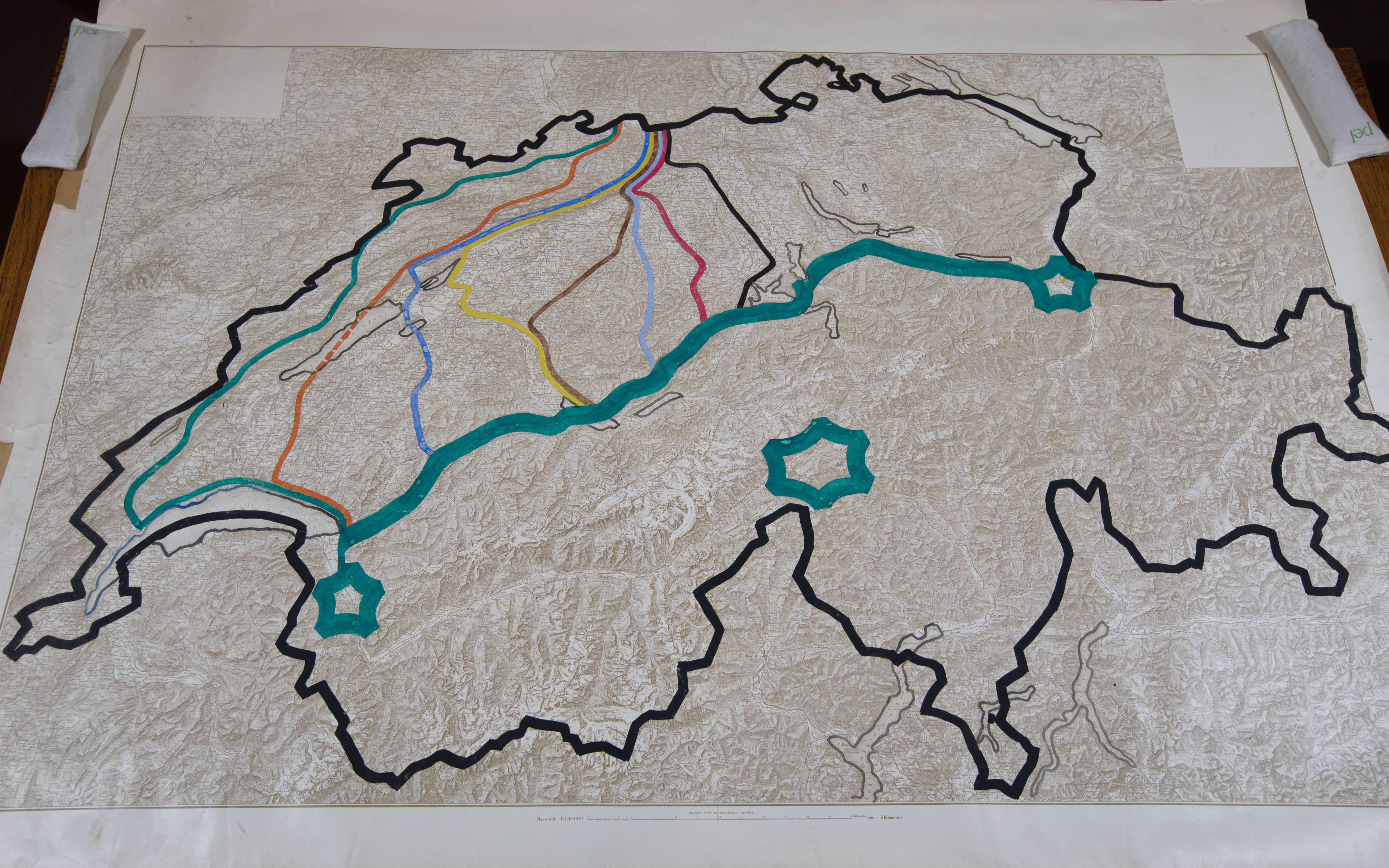 Reliefkarte der Schweiz. Die Landesgrenze ist schwarz markiert. Entlang der  Nordflanke der Alpen ist eine fette türkise Linie gezogen. Sie markiert die Réduitlinie. Die drei Alpenfestungen St. Maurice, Gotthard und Sargans sind markiert. Durchs Mittelland gehen mehrere Verteidigungslinien, die verschiedenfarbig eingezeichnet sind.
