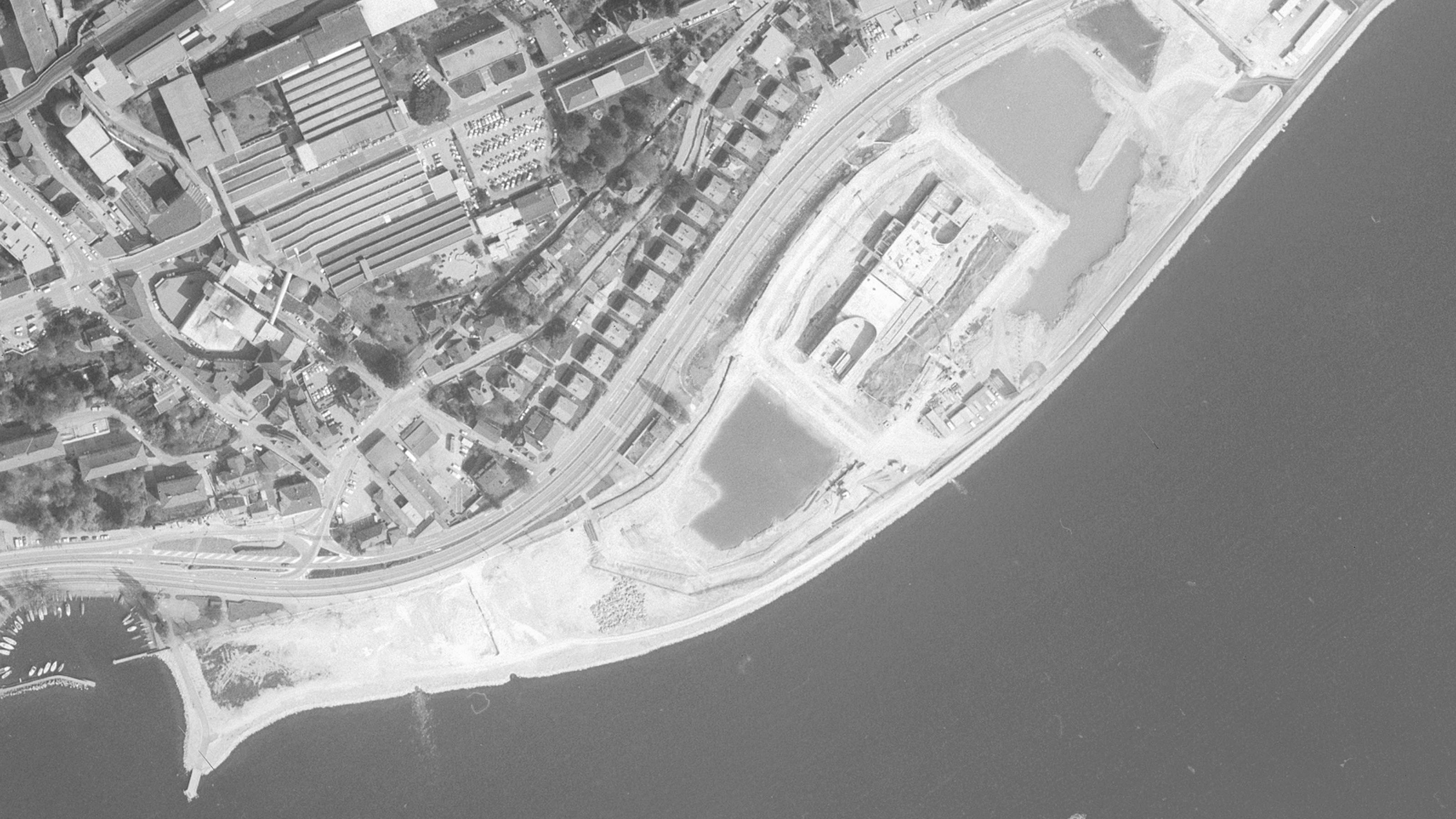 Luftbild von Neuenburg, 1987, schwarzweiss. Die Stadt breitet sich in früheres Seegebiet aus.