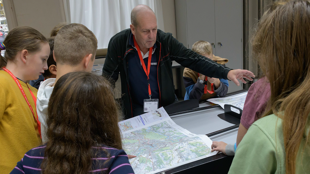 A group of people look at a paper map together, a swisstopo employee gives explanations