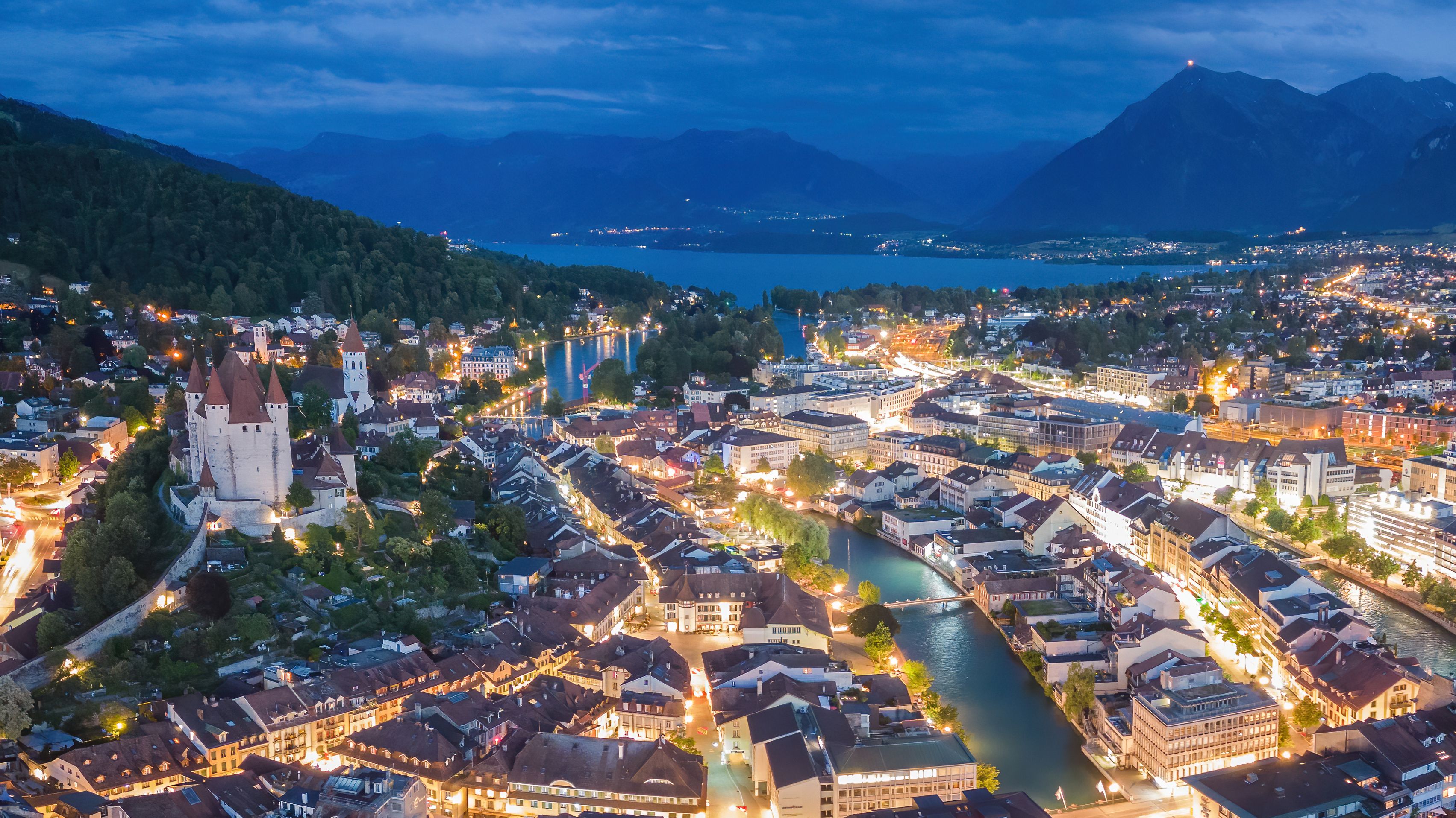 Aerial view of the old town of Thun at night, with Lake Thun and the Bernese Alps in the background.