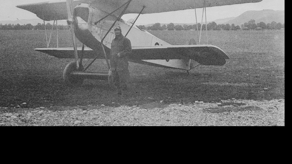 Pilot in front of a biplane on the airfield. Historical photograph.