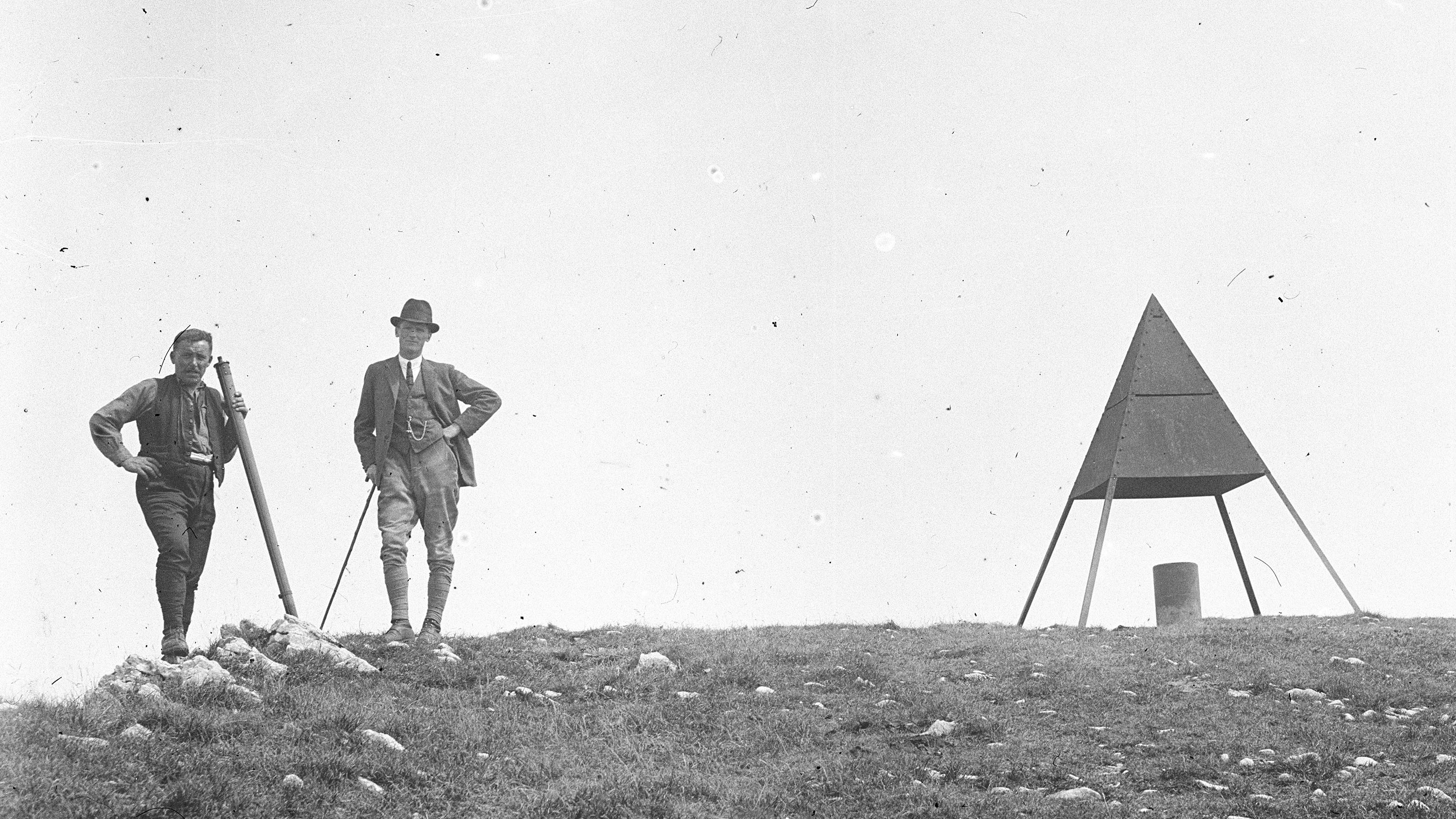 Zwei Vermesser stehen auf dem Gipfel des Chasseral neben einer Vermessungspyramide.