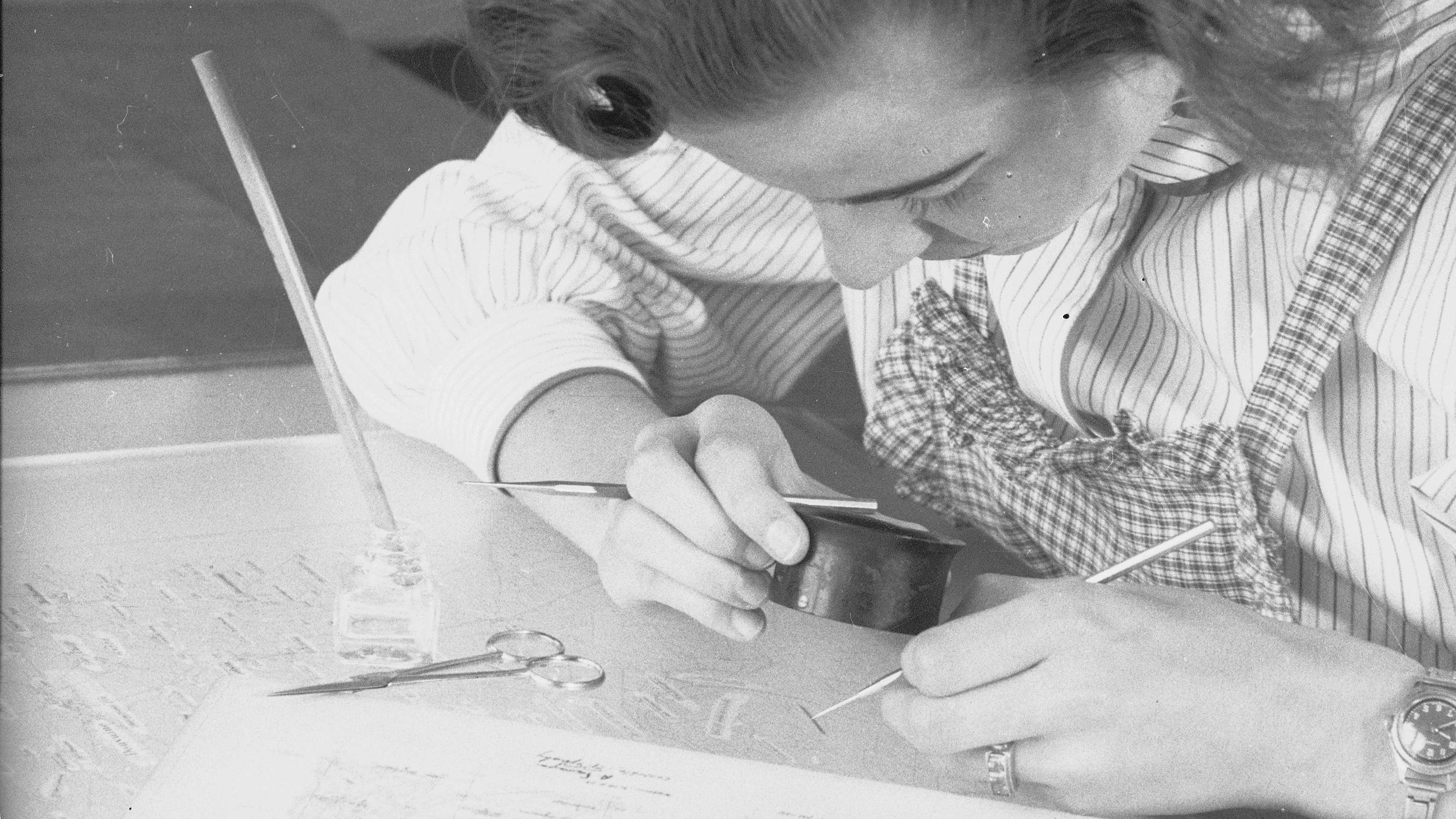 Eine Schriftsetzerin bei der Arbeit über die Glasplatte gelehnt.