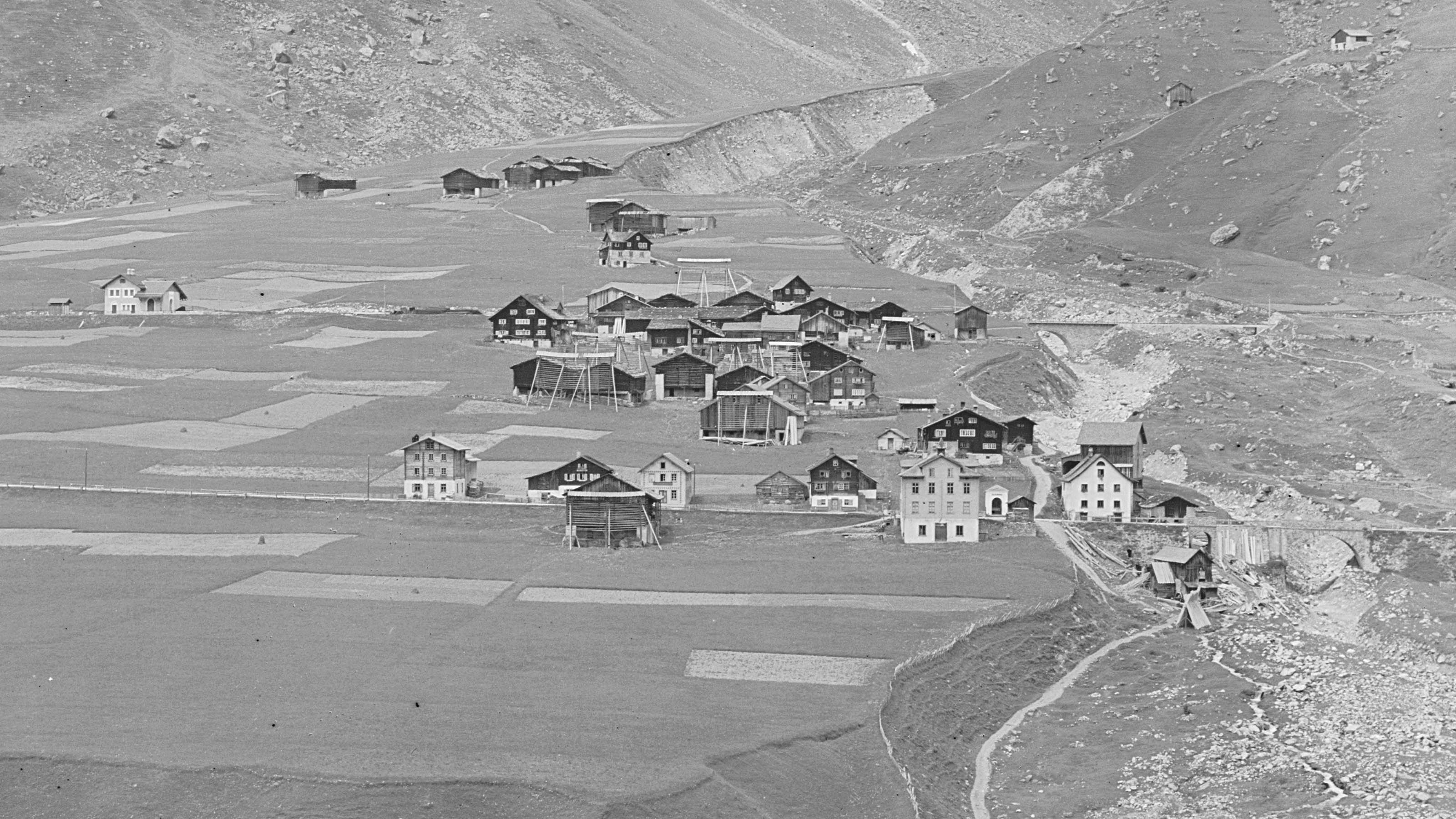 Detail der terrestrischen Aufnahme von Sedrun. Vor den Bauernhäusern stehen Kornhisten. Sie gleichen Gerüsten aus Holz.