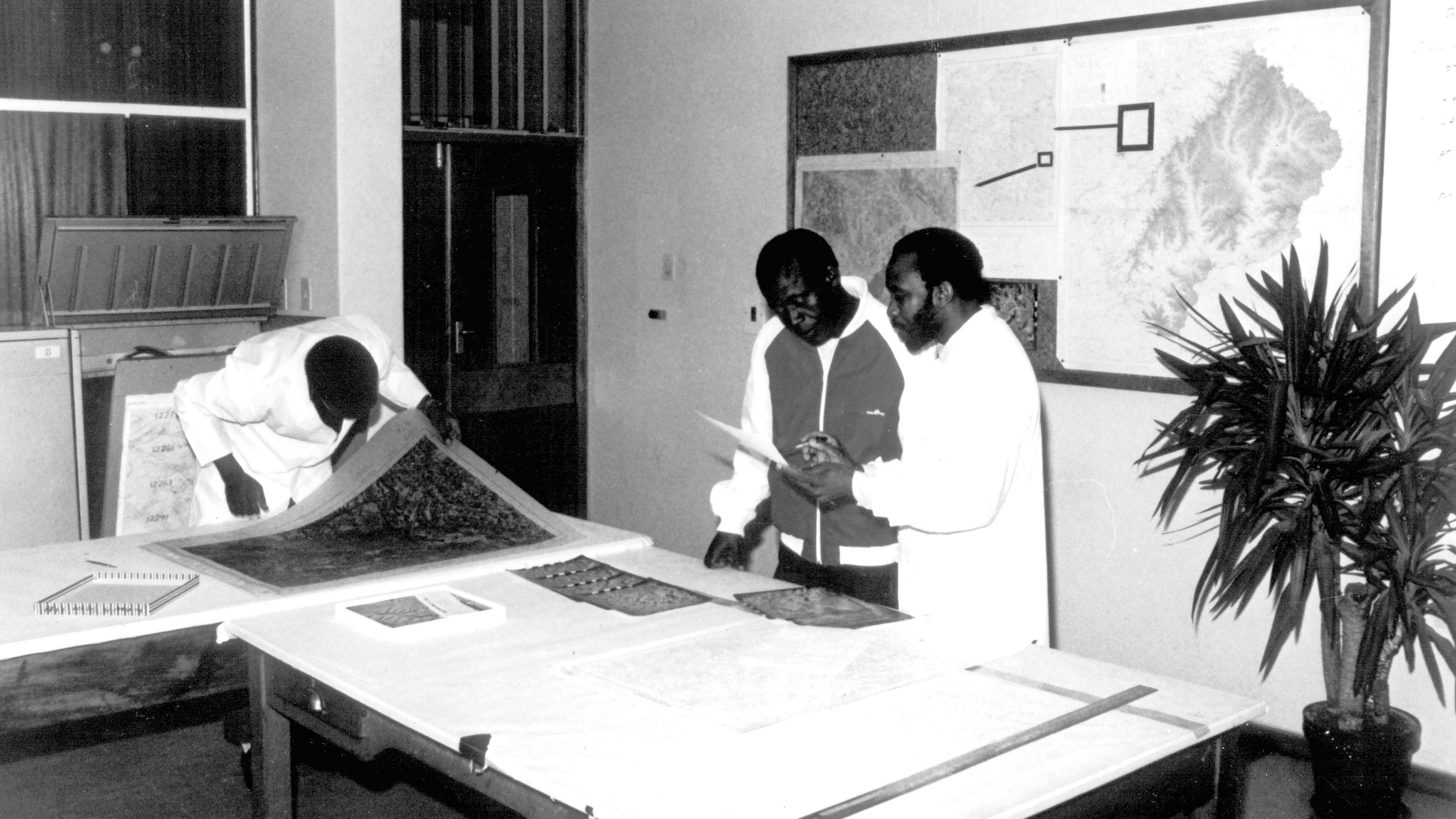 Drei Kartografen aus Lesotho an der Arbeit. An der Wand hängt die Generalkarte Lesothos.