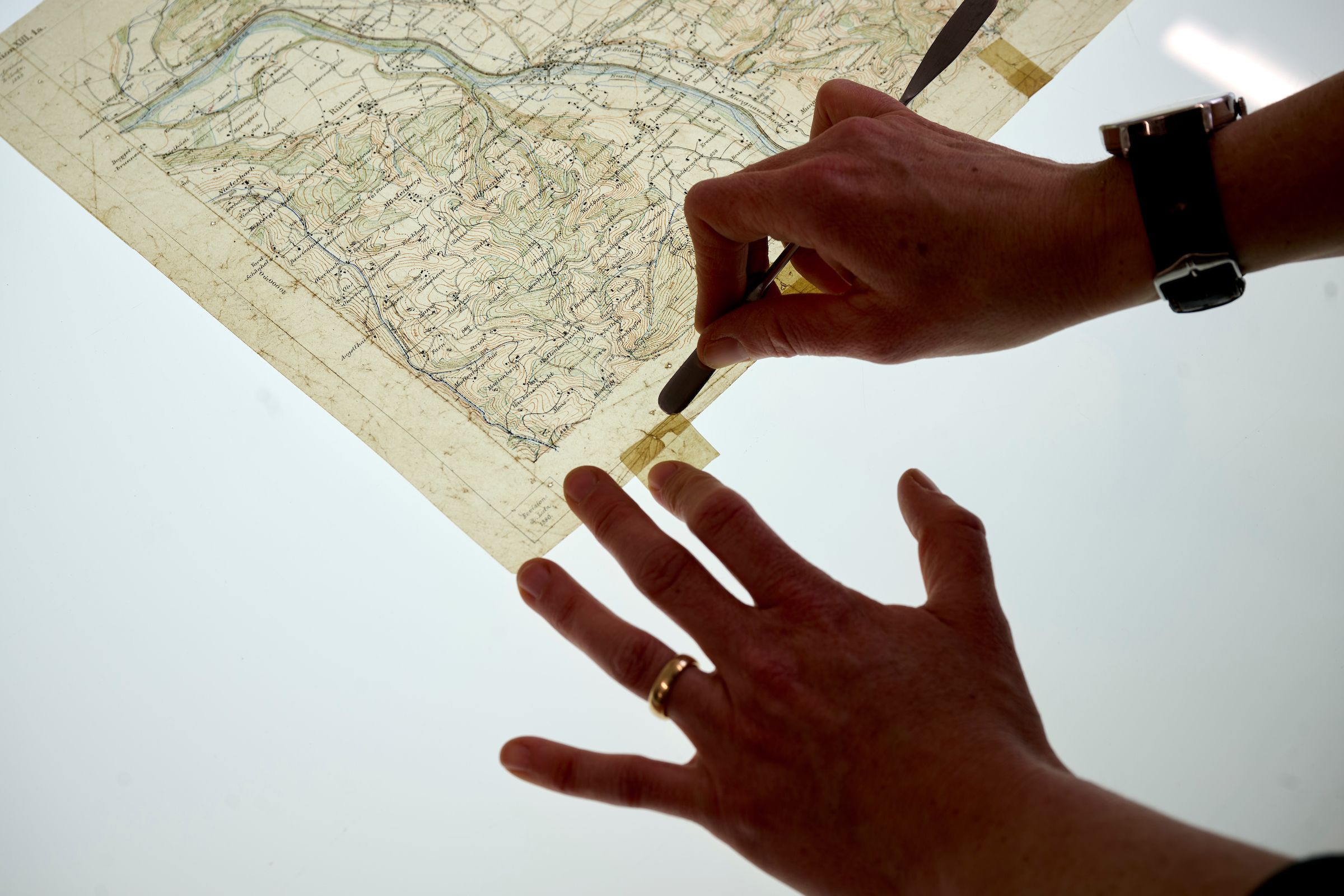 Lea Dauwalder, während sie auf dem beleuchteten Tisch im Atelier eine handgezeichnete Karte auf Transparentpapier restauriert.