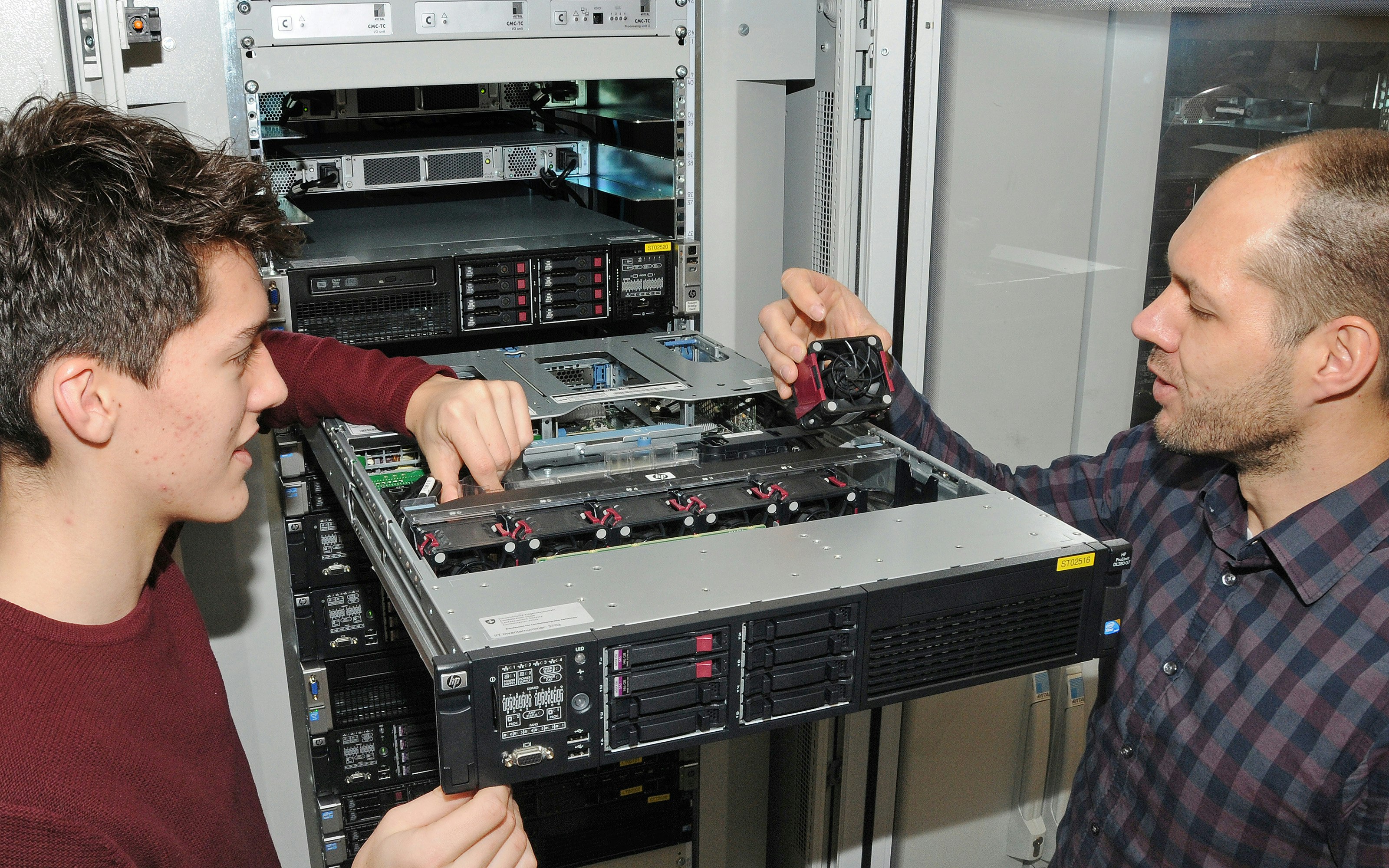 Der Informatiklernende und sein Betreuer wechseln einen Lüfter an einem Server aus.