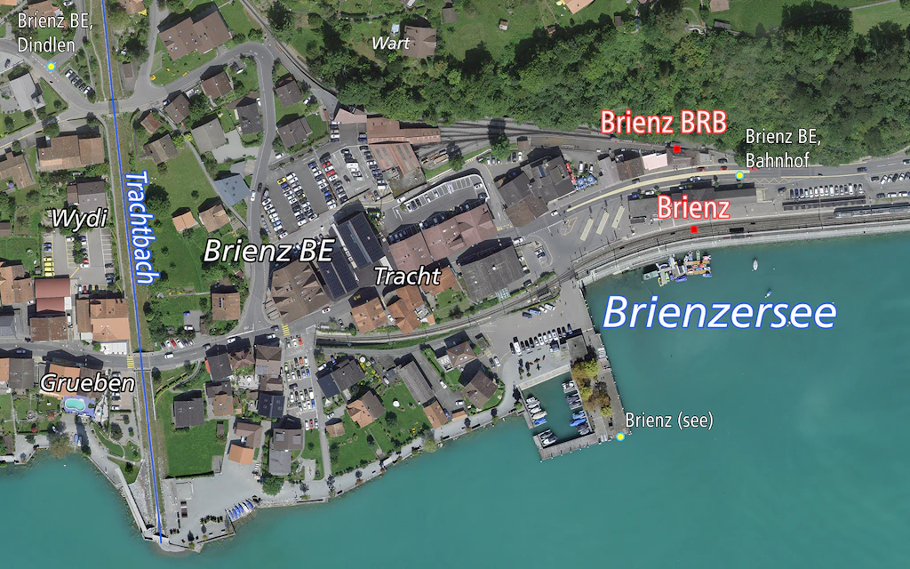 Das Bild zeigt eine Luftaufnahme von Brienz BE mit dem Dorf, dem Bahnhof und dem Brienzersee. 