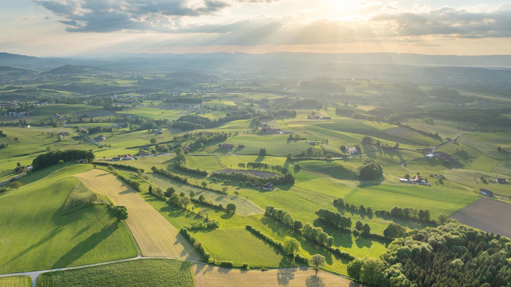 Sensebezirk im Kanton Freiburg im Abendlicht. Landschaft mit Feldern, Hecken und kleinen Siedlungen. Luftaufnahme