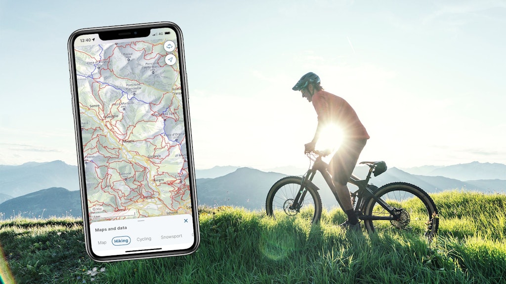 Screen base map with hiking theme in the swisstopo app with a person on a bike in the background