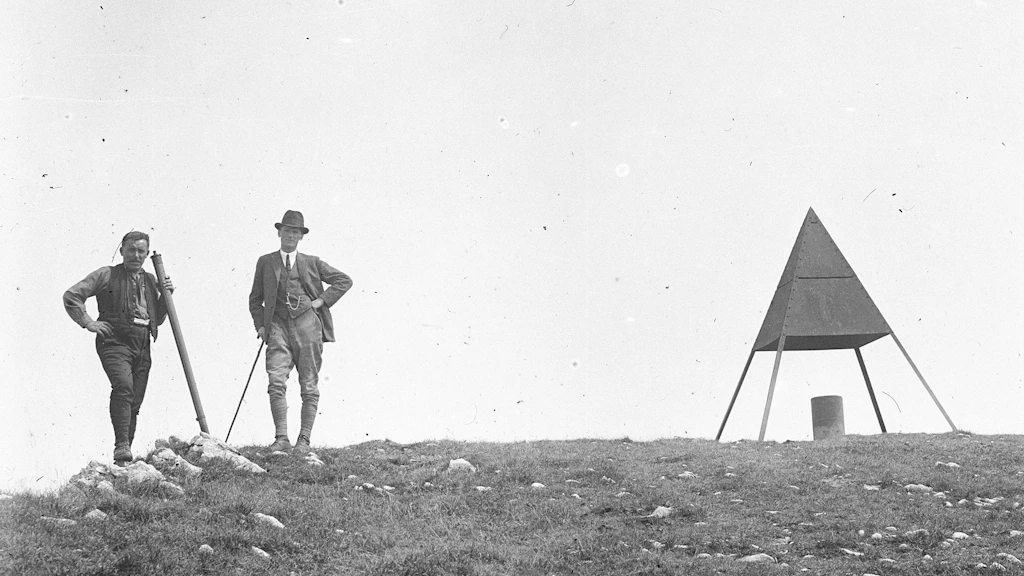 Deux géomètres se tiennent au sommet du Chasseral, à côté d'une pyramide d'arpentage.