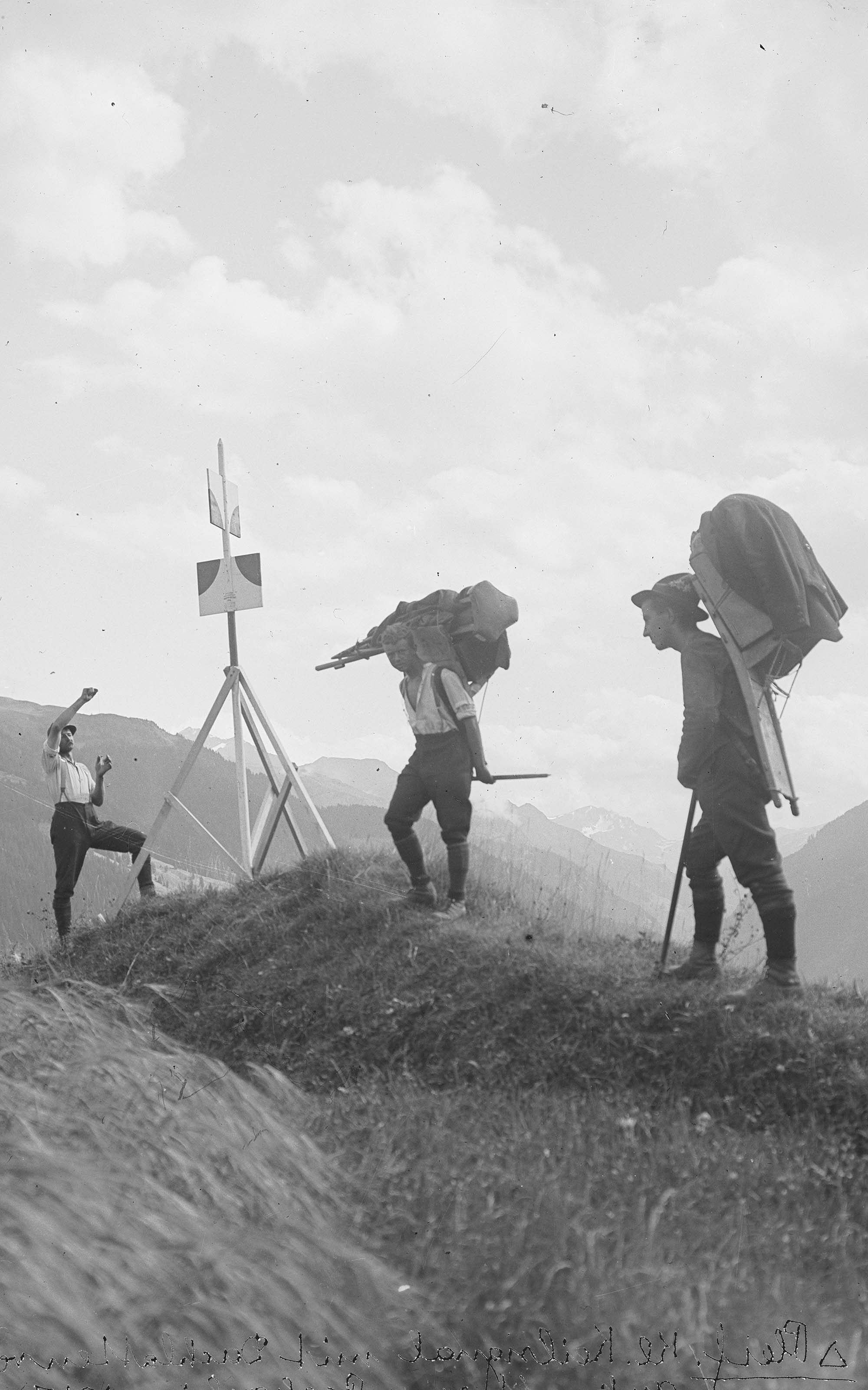 Un ingénieur avec deux assistants lourdement chargés lors d'un signal d'arpentage.
