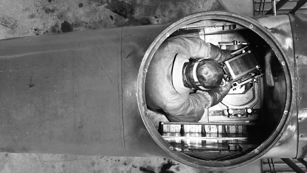 L'immagine mostra un operatore dell'Ufficio federale di topografia su un aereo parcheggiato. Si sta esercitando a manovrare la macchina fotografica aerea in equipaggiamento completo.